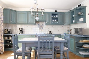 Une cuisine avec des meubles de couleur turquoise, une table à manger avec des chaises, un lustre et divers appareils de cuisine.