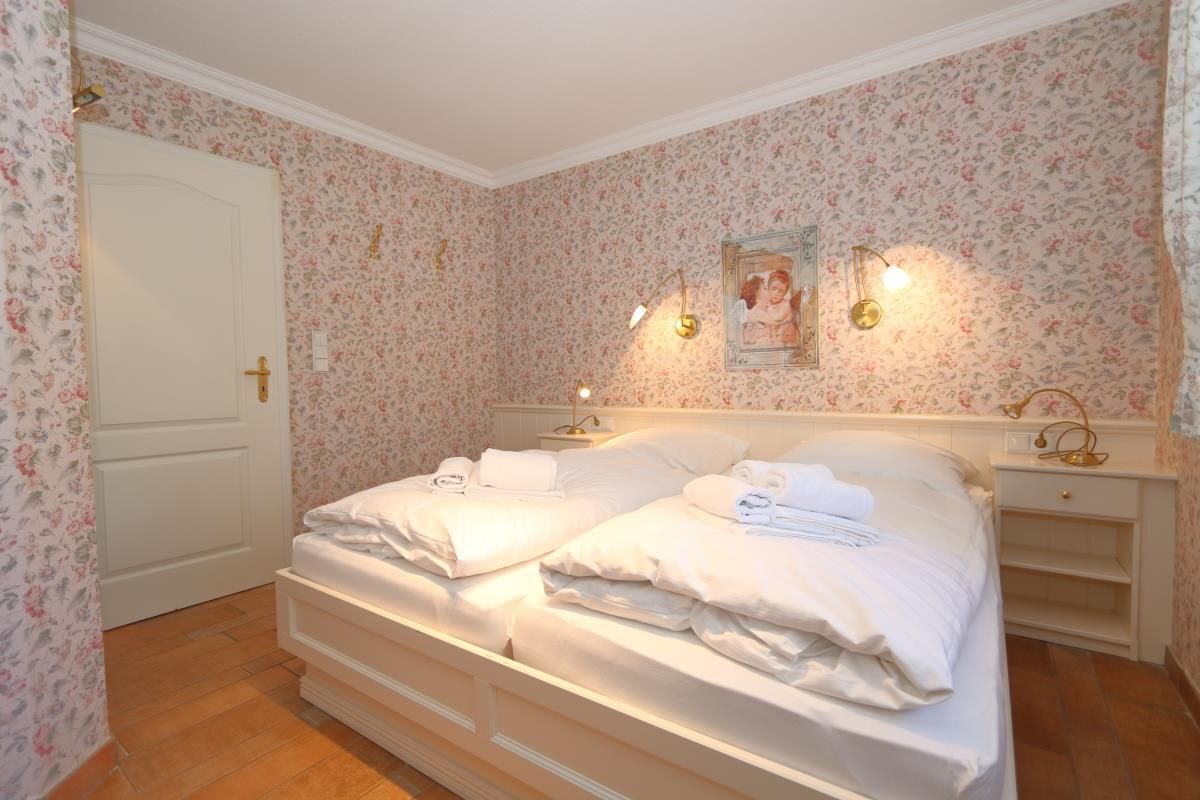 A bedroom with two beds, floral wallpaper, a white door, and bedside lamps.