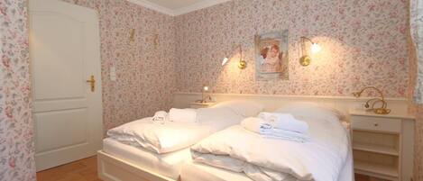 A bedroom with two beds, floral wallpaper, a white door, and bedside lamps.