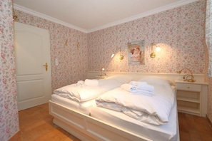 Une chambre avec deux lits, un papier peint à motifs floraux, une porte blanche et des lampes de chevet.