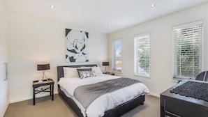 A bedroom with a large bed, two bedside tables, a desk, and a window with blinds. - The Quarter Deck - This riverfront townhouse is modern, fresh and spacious (Port Fairy)