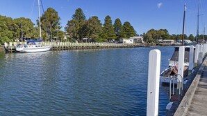 A marina with a docked boat, a wooden pier, and trees in the background. - The Quarter Deck - This riverfront townhouse is modern, fresh and spacious (Port Fairy)