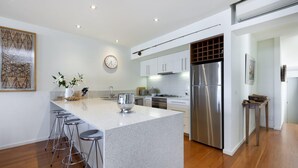 A modern kitchen with a central island, stainless steel appliances, and bar stools. - The Quarter Deck - This riverfront townhouse is modern, fresh and spacious (Port Fairy)