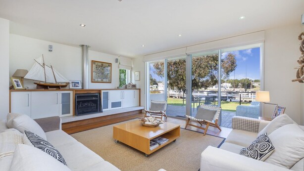 A spacious living room with a fireplace, comfortable seating, and a view of the marina. - The Quarter Deck - This riverfront townhouse is modern, fresh and spacious (Port Fairy)
