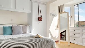 Een slaapkamer met een bed, nachtkastje, spiegel en een bord aan de muur.