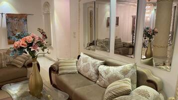 Una sala de estar con un sofá color beige, almohadones decorativos, una mesa de centro de vidrio y un jarrón con flores.