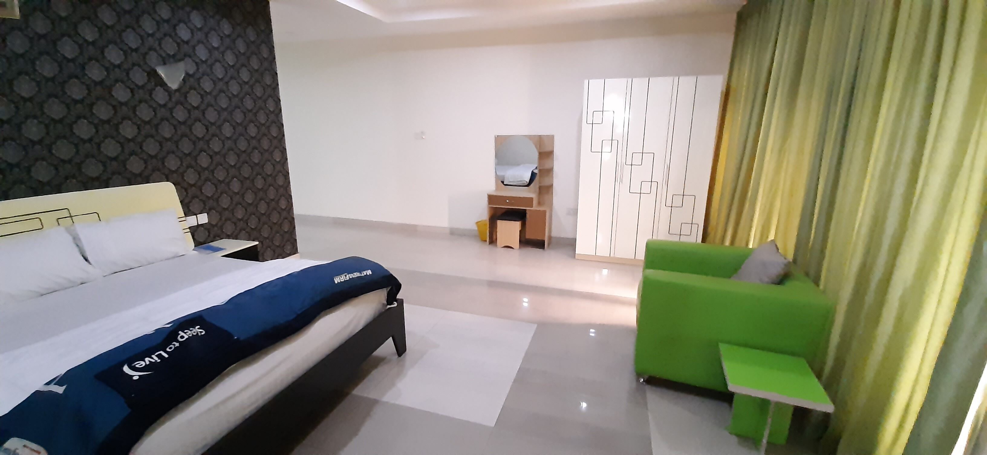 A hotel room with a bed, a green sofa, a small table, and a mirror.