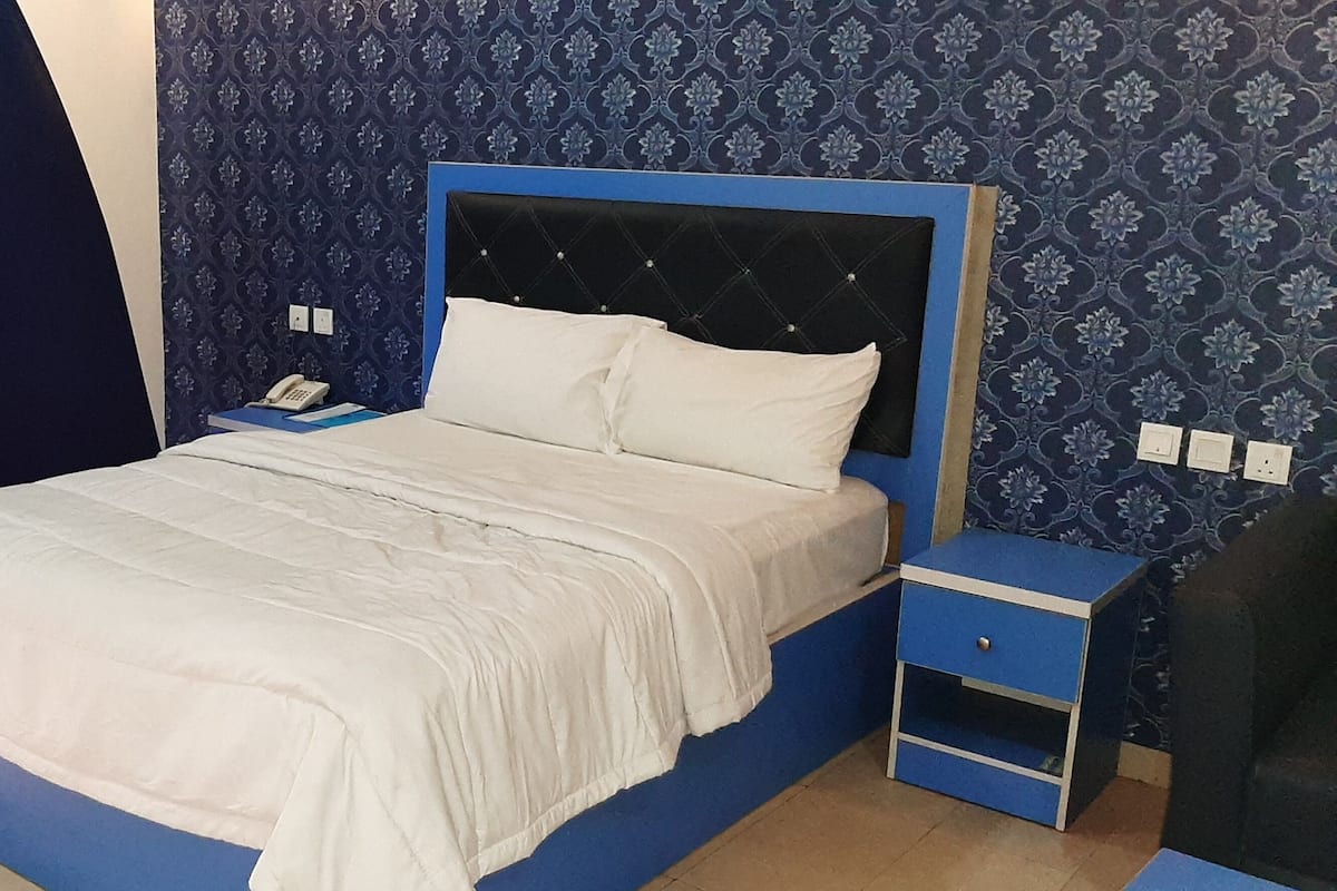 A bedroom with a bed, a nightstand, a blue bedside table, and a patterned wallpaper.