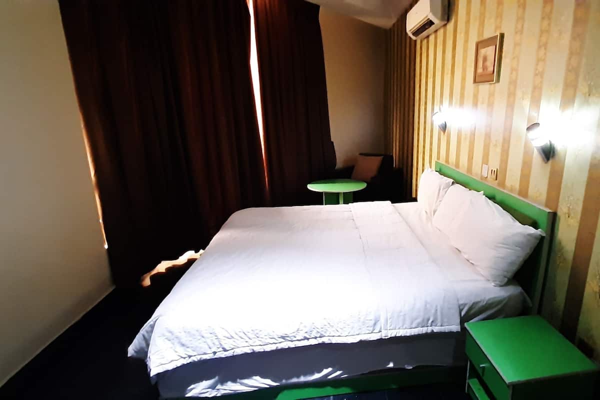 A hotel room with a bed, a green nightstand, a small table, and a wall-mounted light fixture.