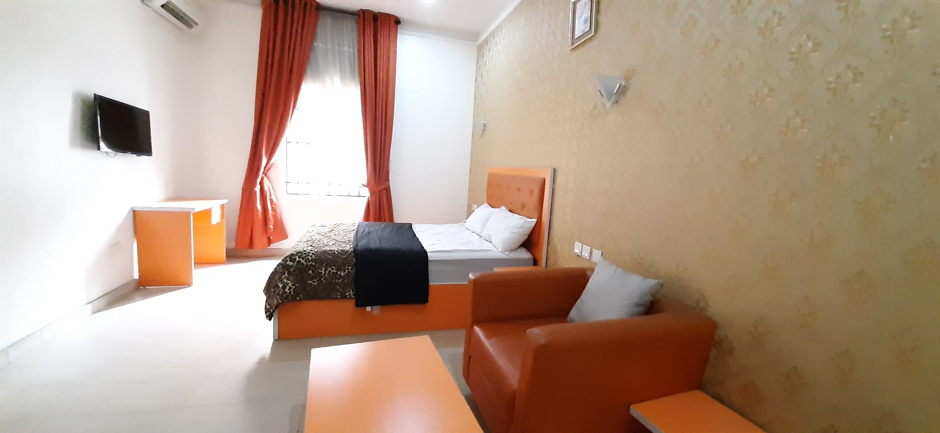 Habitación de hotel con cama, sofá, televisor y ventana con cortinas.