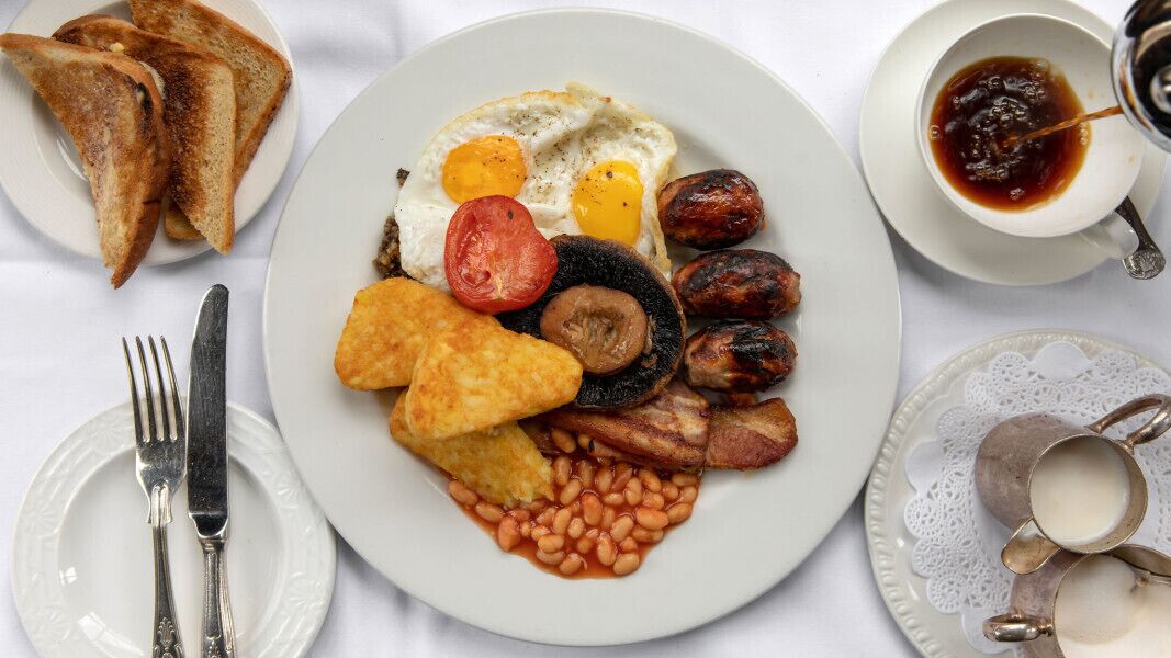 A breakfast plate with eggs, sausages, beans, toast, and a cup of tea.