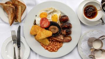 A breakfast plate with eggs, sausages, beans, toast, and a cup of tea.