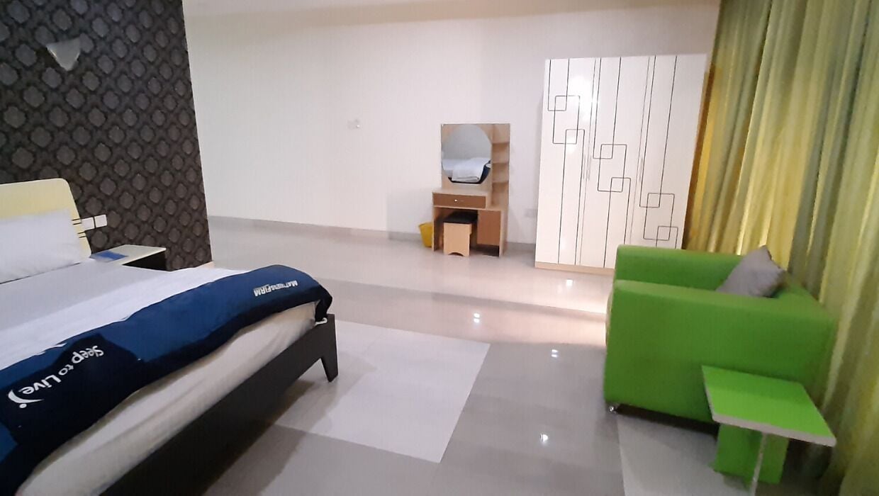 Una habitación de hotel moderna con cama, un sofá verde, una mesita, un espejo y un armario.