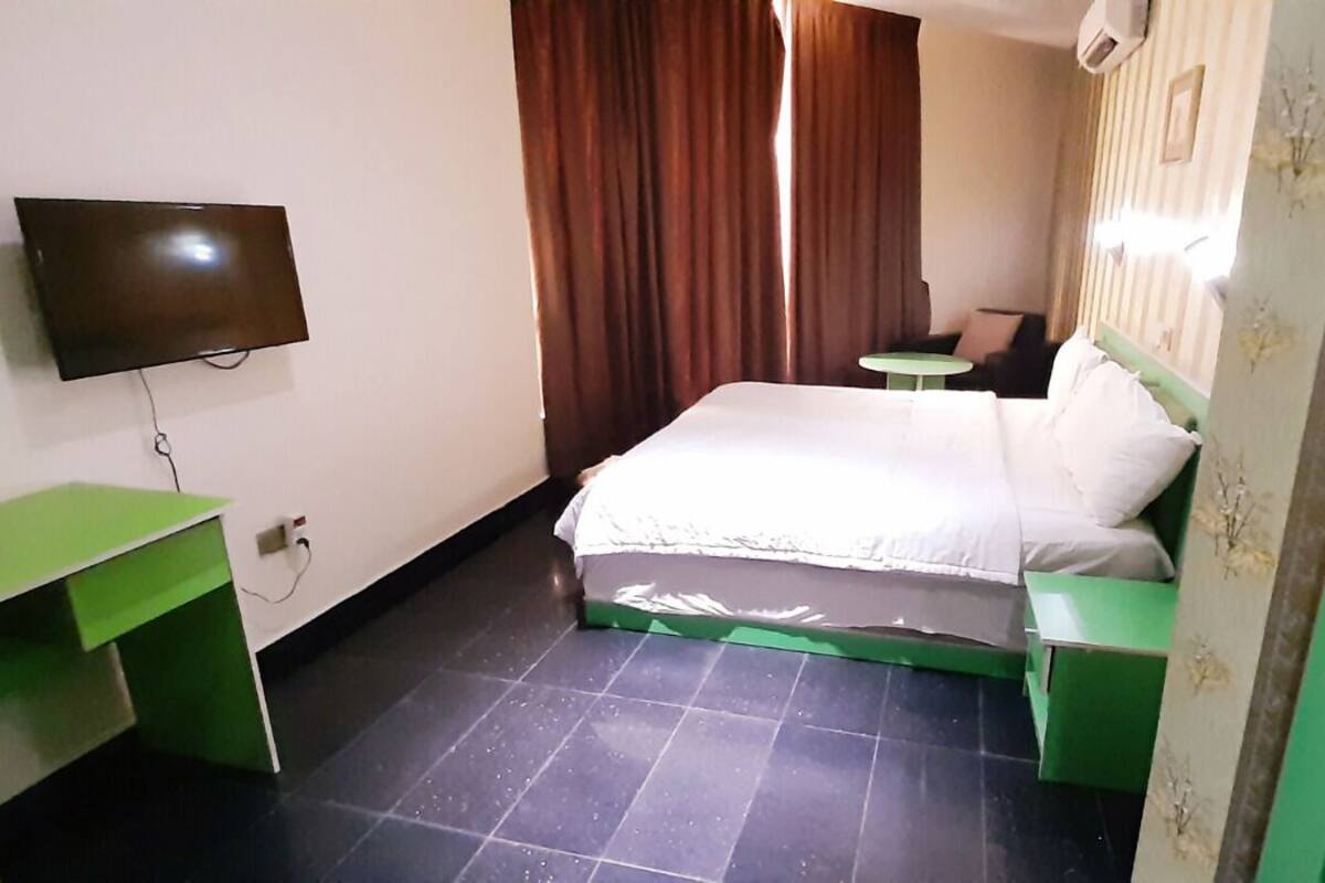 A hotel room with a bed, a TV, a small table, and a curtain.