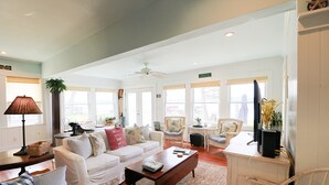 A spacious living room with a white sofa, a coffee table, and a television. There are several chairs and a large window providing natural light. - Beautiful lakefront cottage on Chautauqua Lake in a quiet setting! (Jamestown)