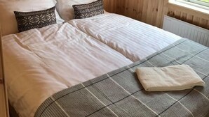 Ein Doppelbett mit weißen und gemusterten Kissen, einer Karo-Decke und einem Fenster mit Blick ins Grüne.
