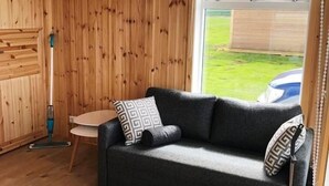 Ein gemütliches Zimmer mit Holzvertäfelung, einer Couch mit gemusterten Kissen, einem kleinen Tisch und einem Fenster mit Blick ins Freie.