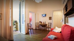 A cozy living room with a red sofa, a dining table with chairs, and a television on the wall. - Green Nest Apartaments - GREEN NEST (Florence)