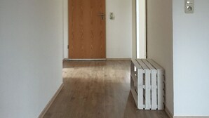 A hallway with wooden flooring, a wooden door at the end, a ceiling light, and a wall-mounted light switch.