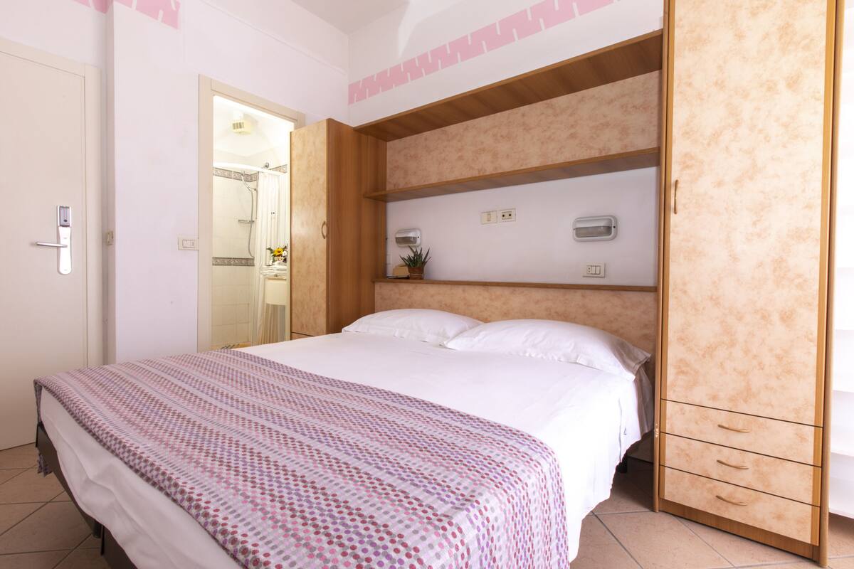 A bedroom with a bed, a wardrobe, and a bathroom visible through an open door.