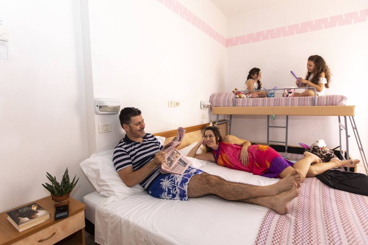 A room with a bunk bed, a bedside table with a plant, and a person reading a book.