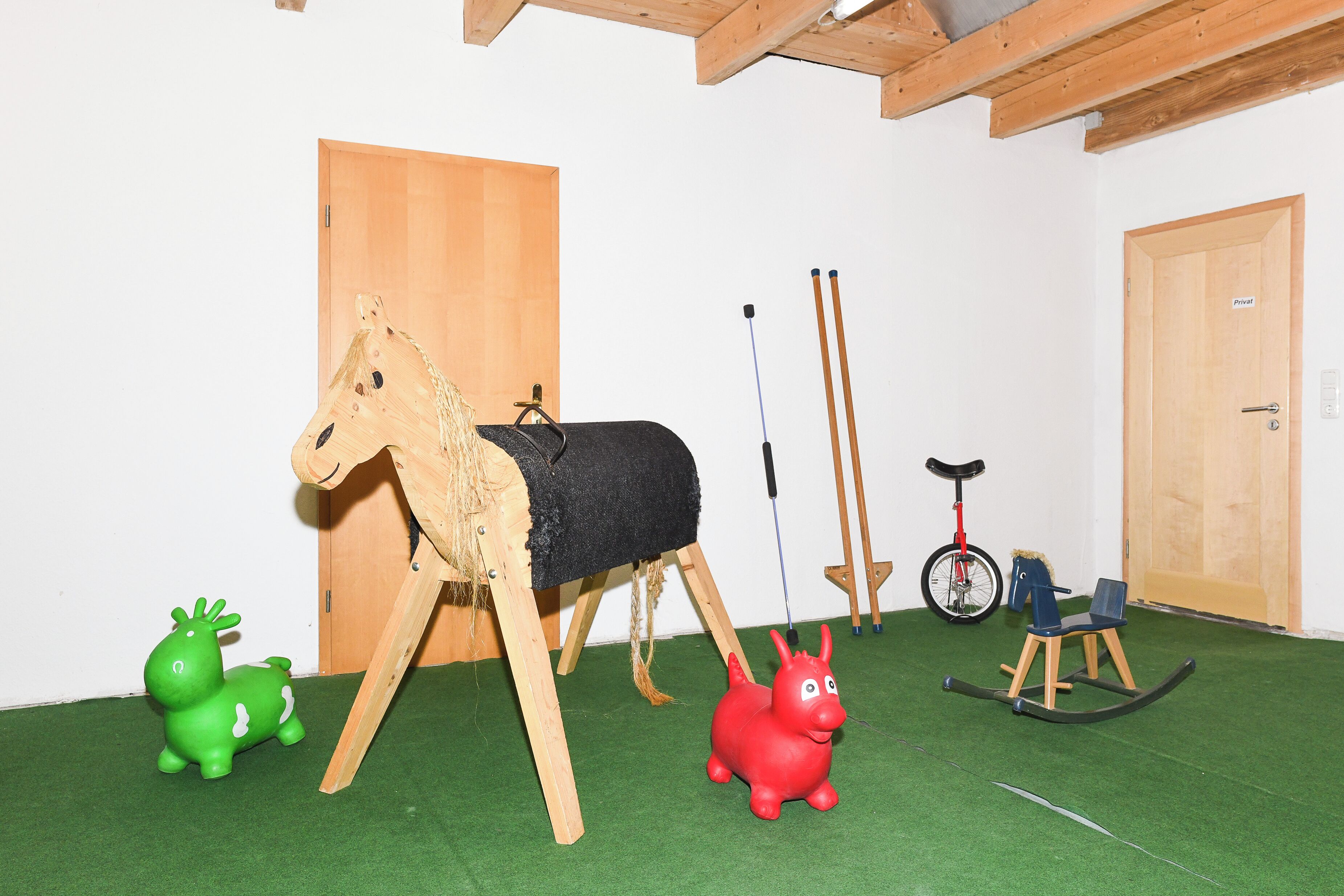 Una habitación con una escultura de caballo de madera, un caballo de juguete verde y rojo, una mecedora y un triciclo.