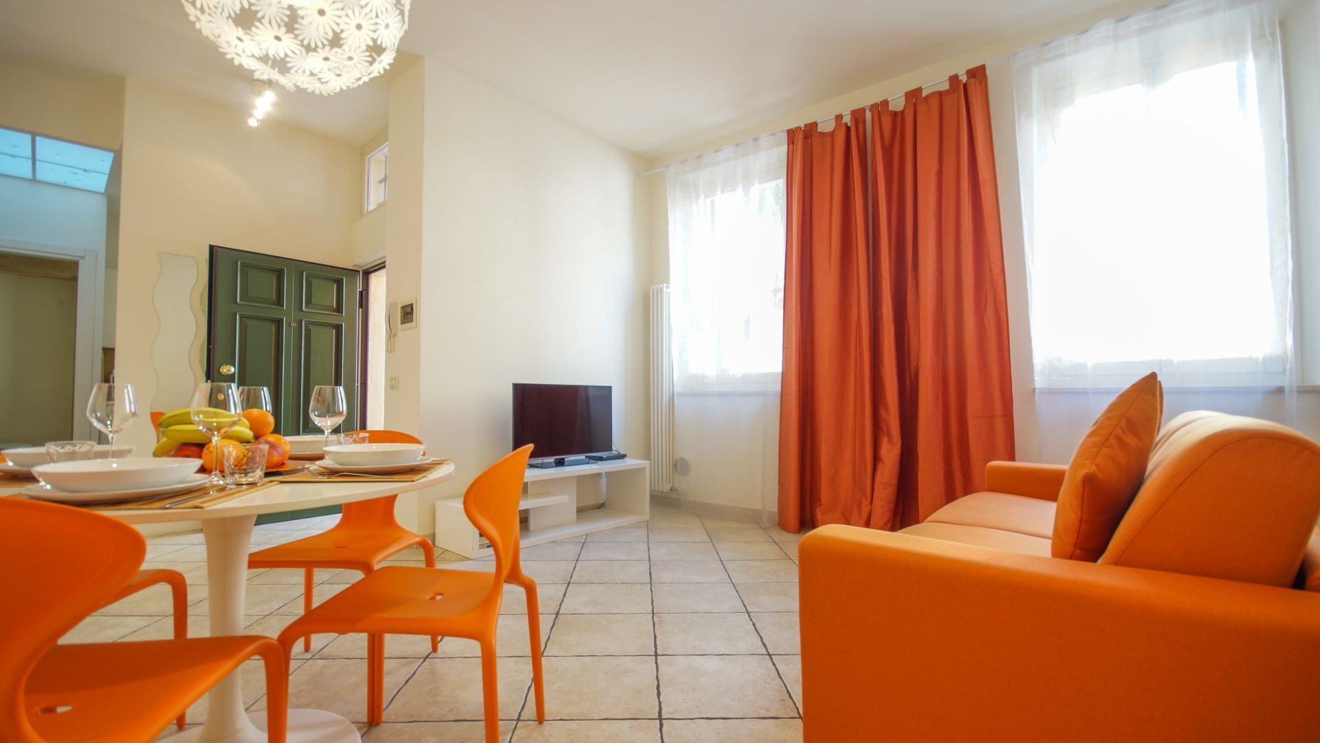 Un soggiorno moderno con arredamento arancione, una zona pranzo con tavolo apparecchiato per due e un televisore.