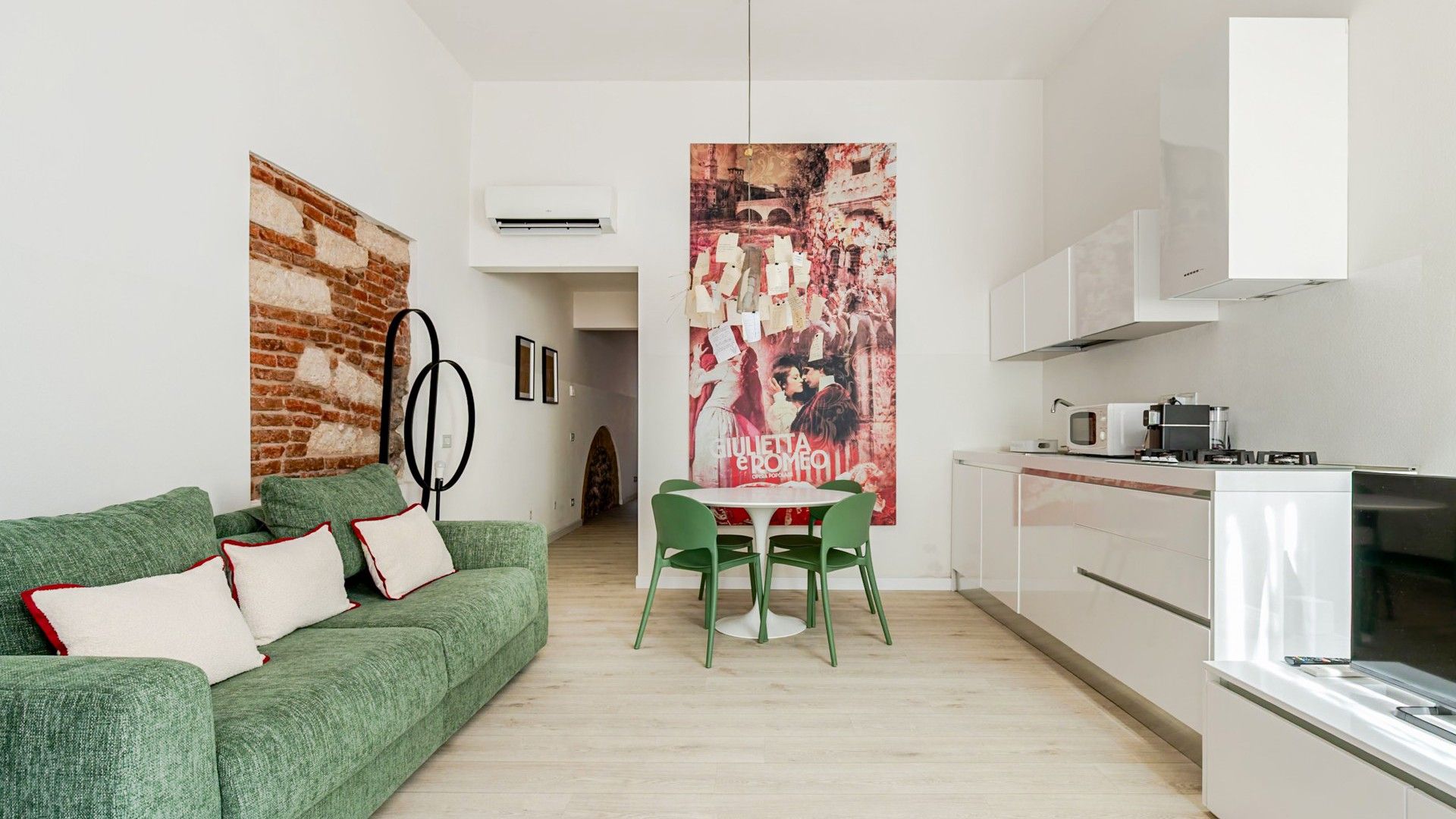 Um apartamento moderno com um sofá verde, uma mesa de jantar com cadeiras, uma área de cozinha e um pôster grande na parede.