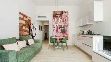 Un appartement moderne avec un canapé vert, une table à manger avec des chaises, un coin cuisine et une grande affiche accrochée au mur.