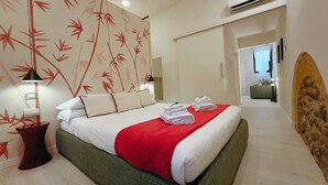 Una habitación de hotel con cama, almohadas, una manta roja y toallas.