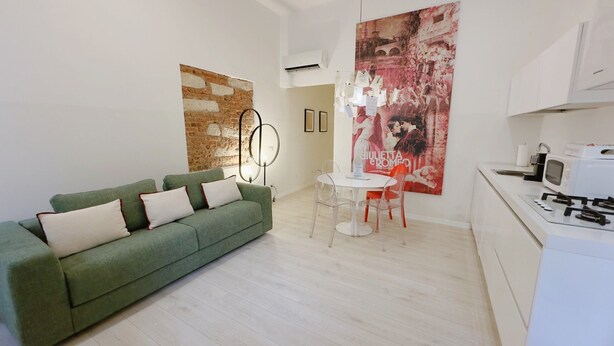 Una sala de estar moderna con un sofá verde, una mesa de comedor con sillas y una cocina con estufa y microondas.