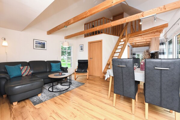 A modern living room with a black leather sofa, a dining table with chairs, wooden flooring, and a staircase leading to an upper level. - For families and those looking for peace, non-smoking apartment, free WiFi (Wittmund)