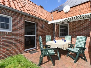 Une maison en briques avec un toit en tuiles, une antenne parabolique et une terrasse avec une table et des chaises.