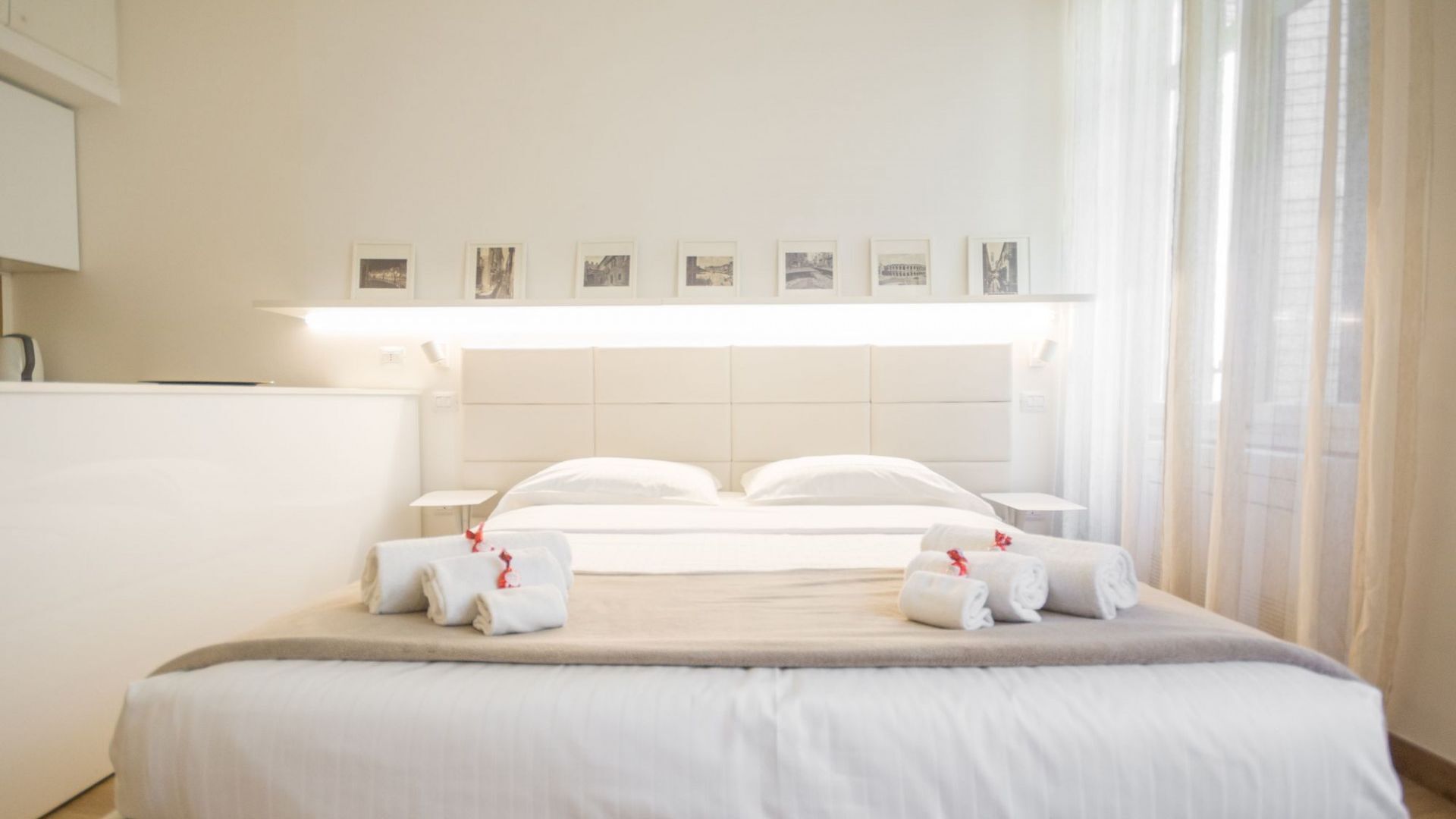 Ein Hotelzimmer mit einem großen Bett, zwei Nachttischen, einem Kunstwerk-verzierten Kopfteil und einem fenster mit Vorhängen.