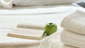 Una cama con una manzana verde, un libro y toallas dobladas.