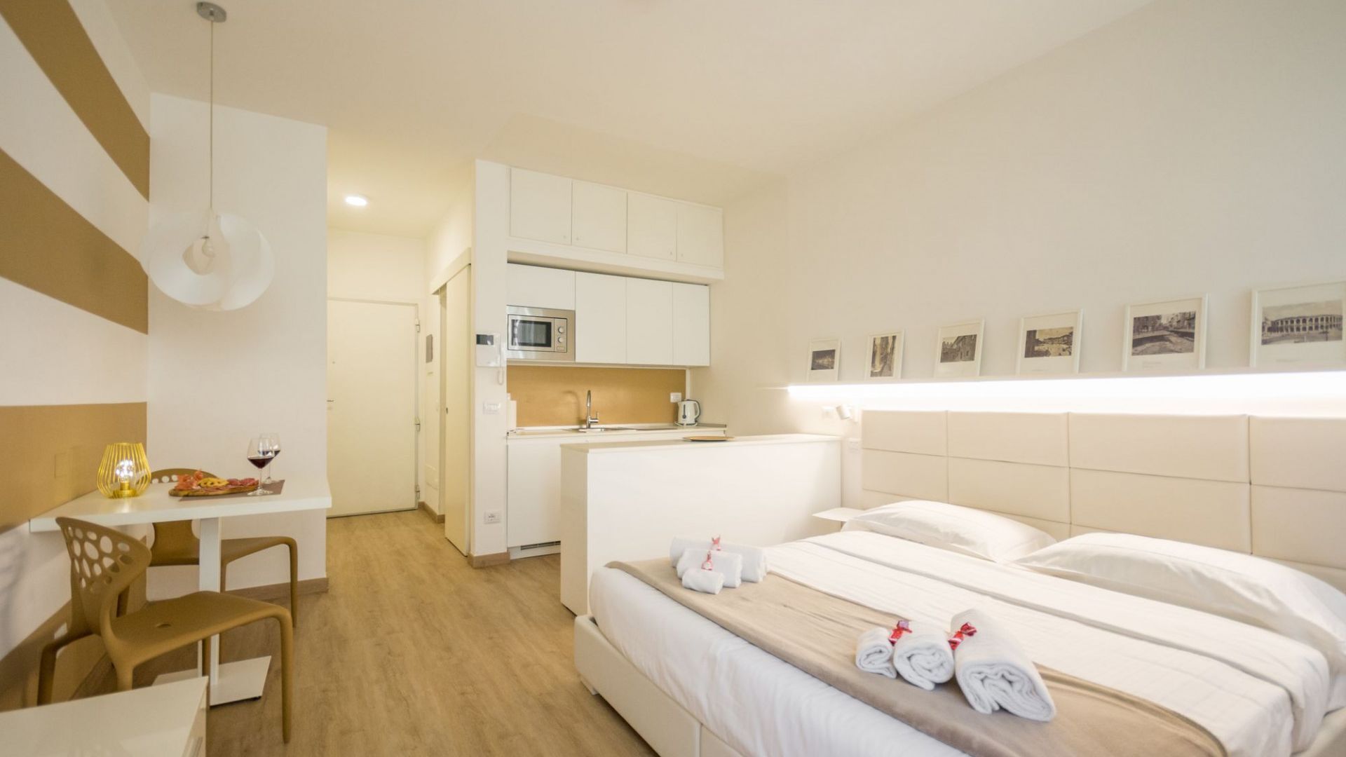 A hotel room with a bed, a desk, a chair, a kitchenette, and a bathroom.