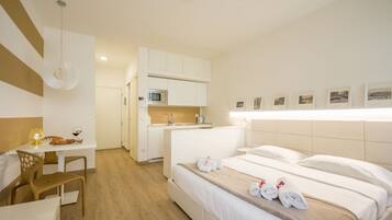 A hotel room with a bed, a desk, a chair, a kitchenette, and a bathroom.