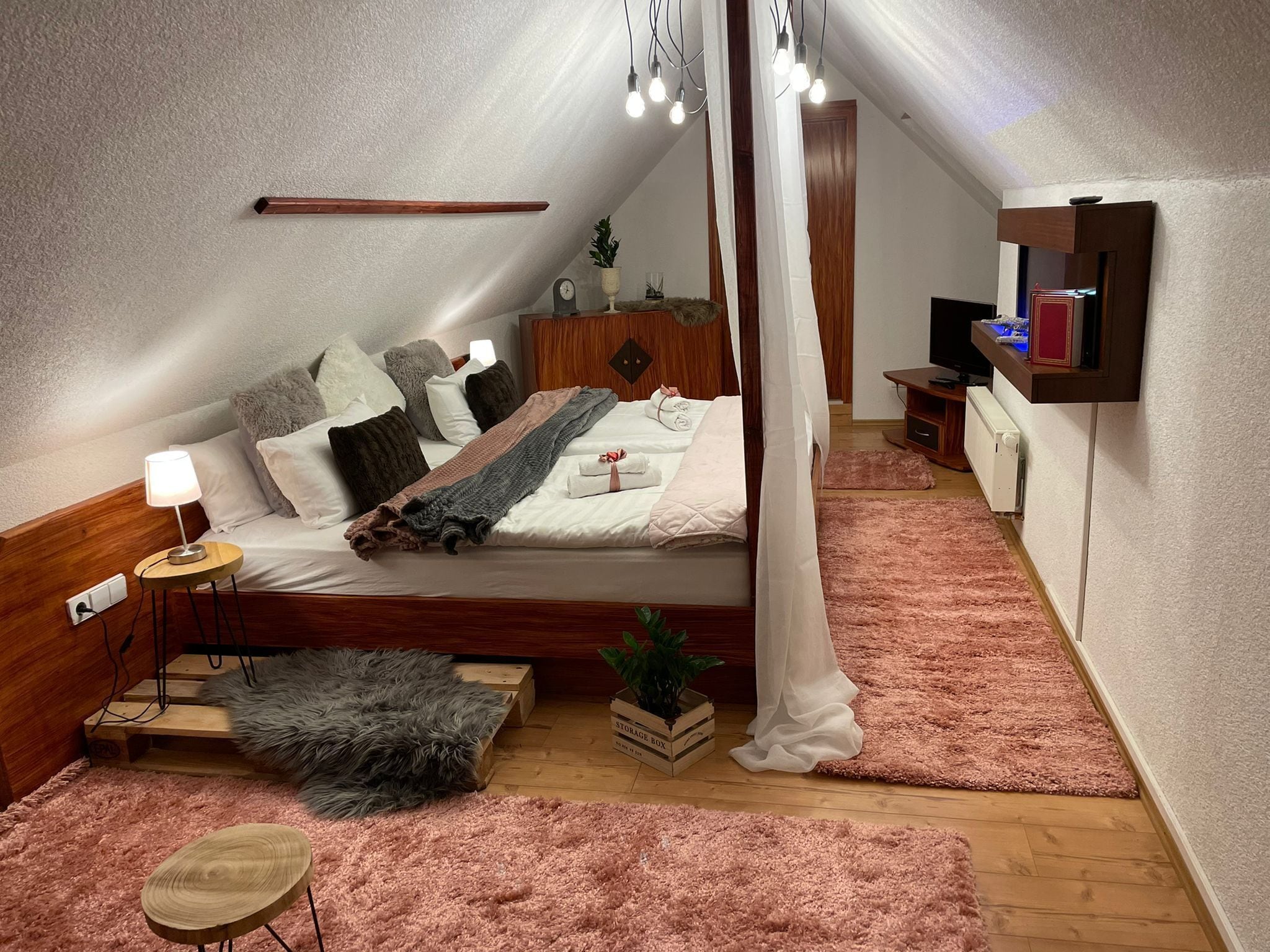 A bedroom with a bed, bedside table, lamp, bedside plant, and a wooden headboard.