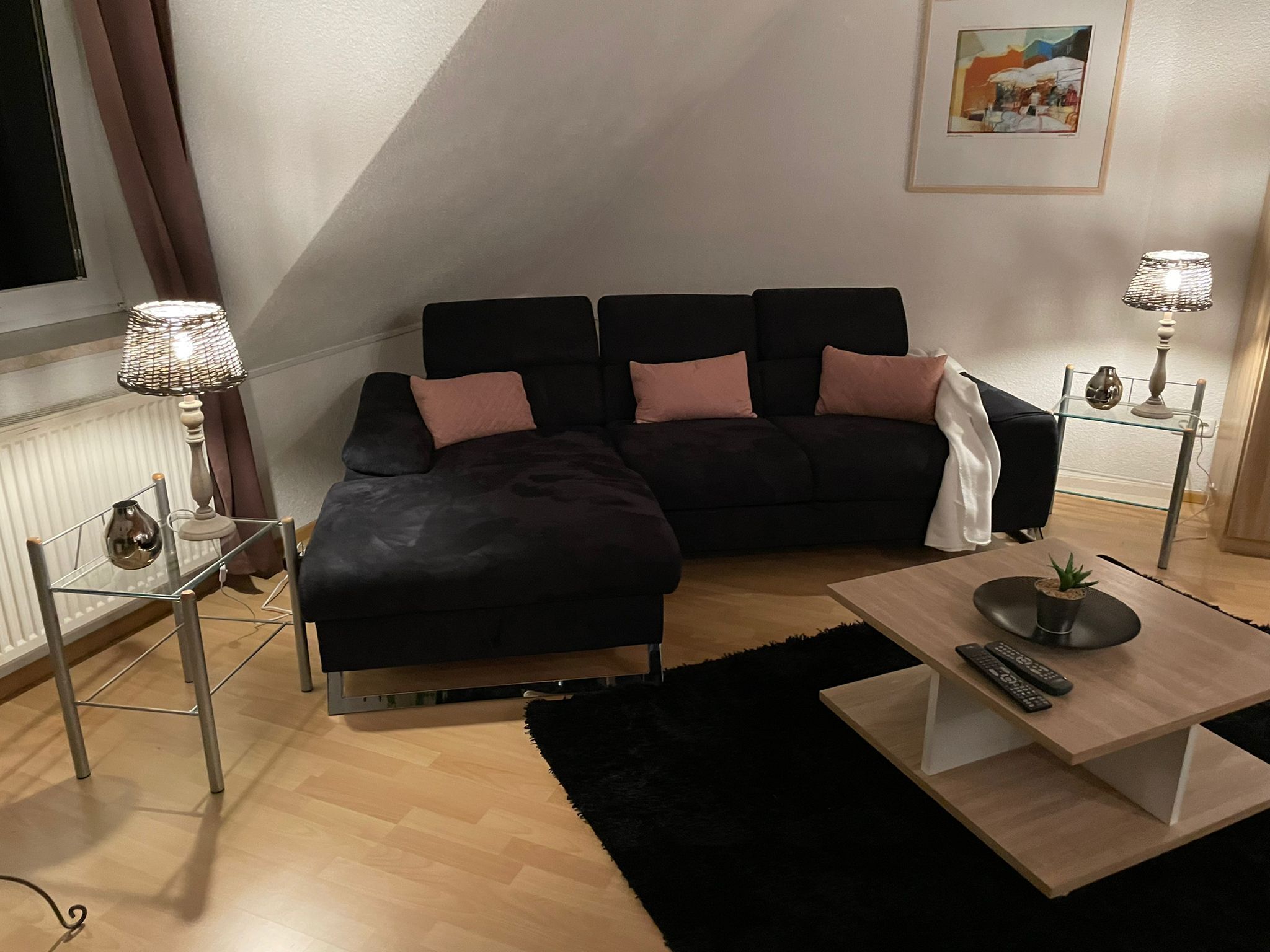 Una sala moderna con un sofá modular negro, una mesa de centro de cristal, un tapete negro y dos lámparas de noche.
