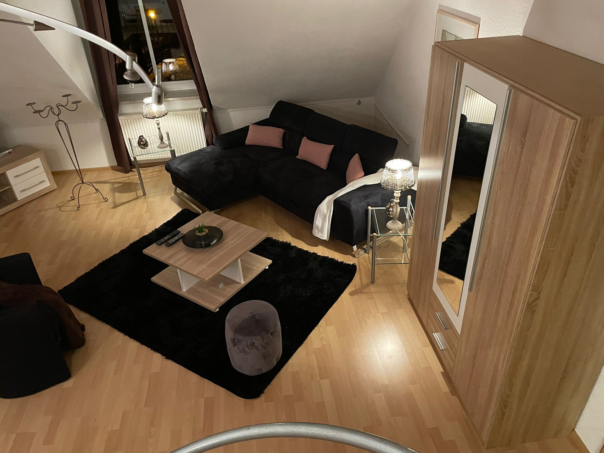 Una sala de estar moderna con un sofá seccional negro, una mesita de centro de madera, una alfombra negra y un mueble espejo.