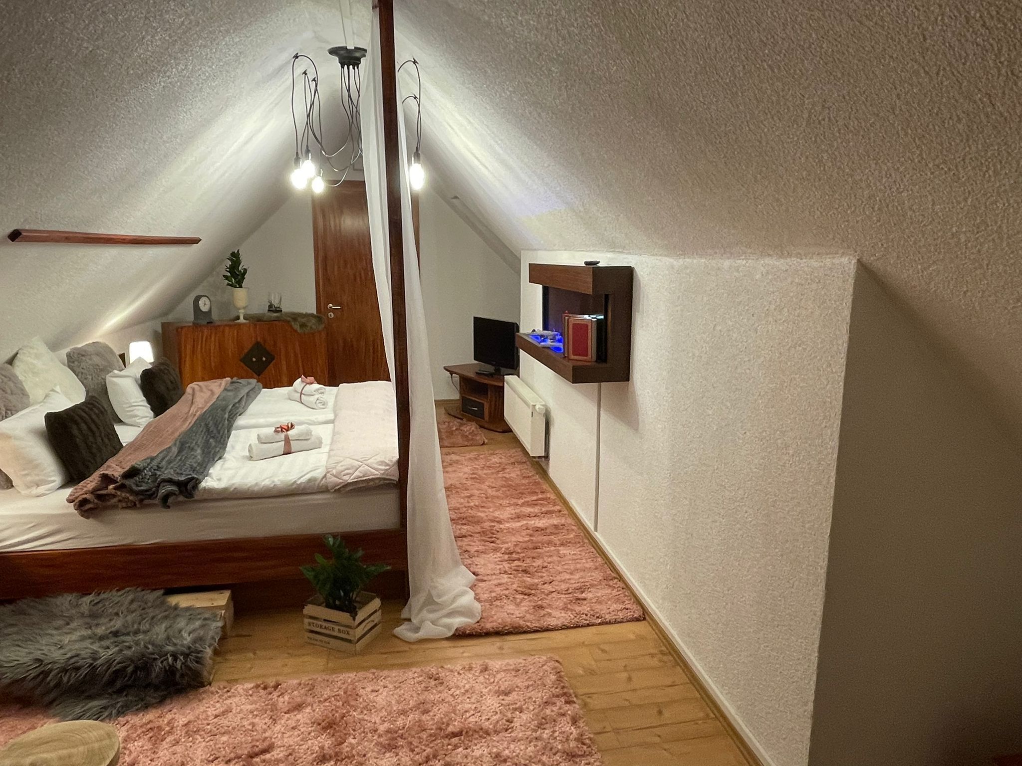 A bedroom with a bed, bedside table, TV, storage box, and a ceiling fan.