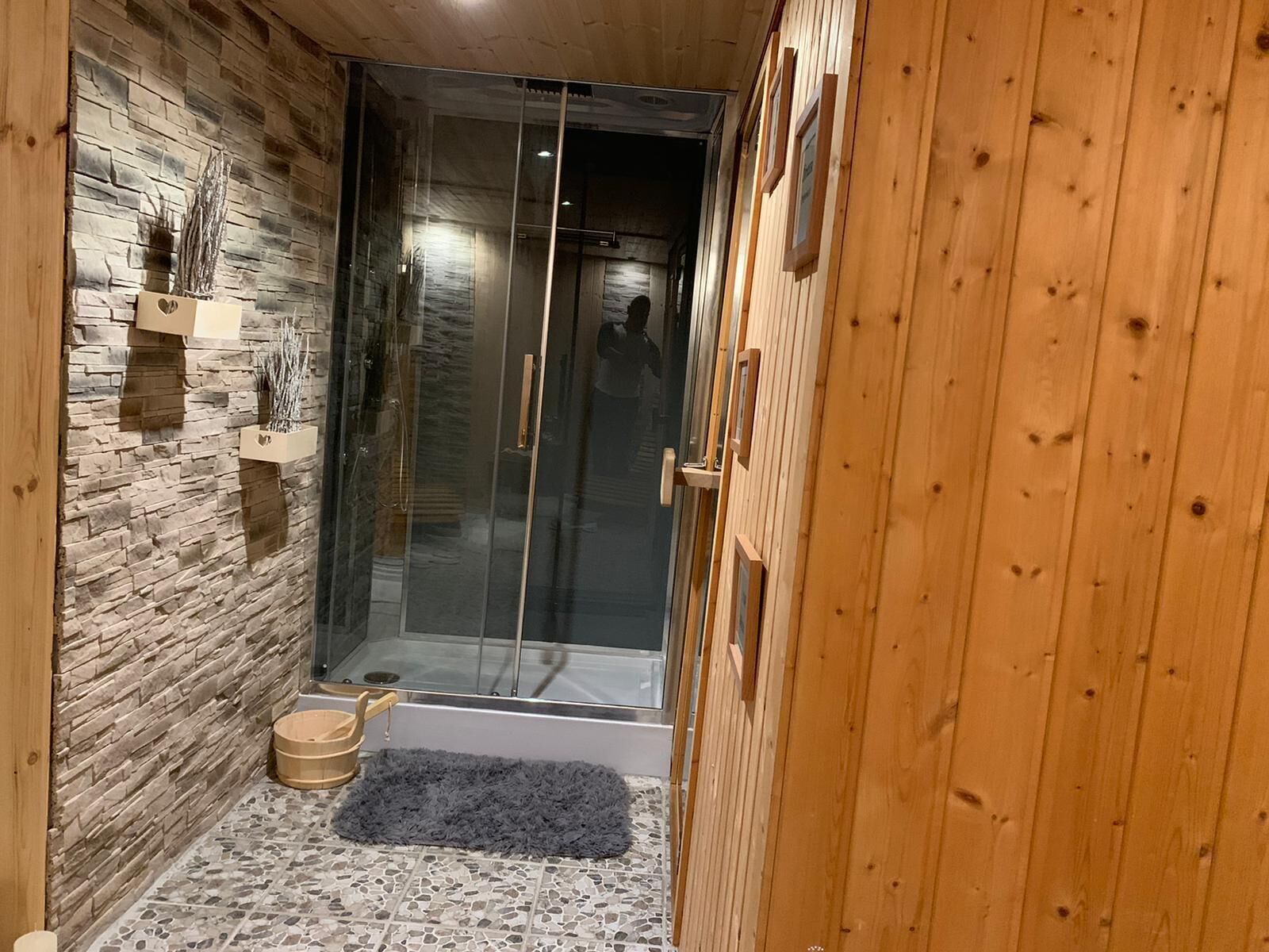 Un espacio de ducha estrecho con puerta de vidrio, pared de piedra y paneles de madera.