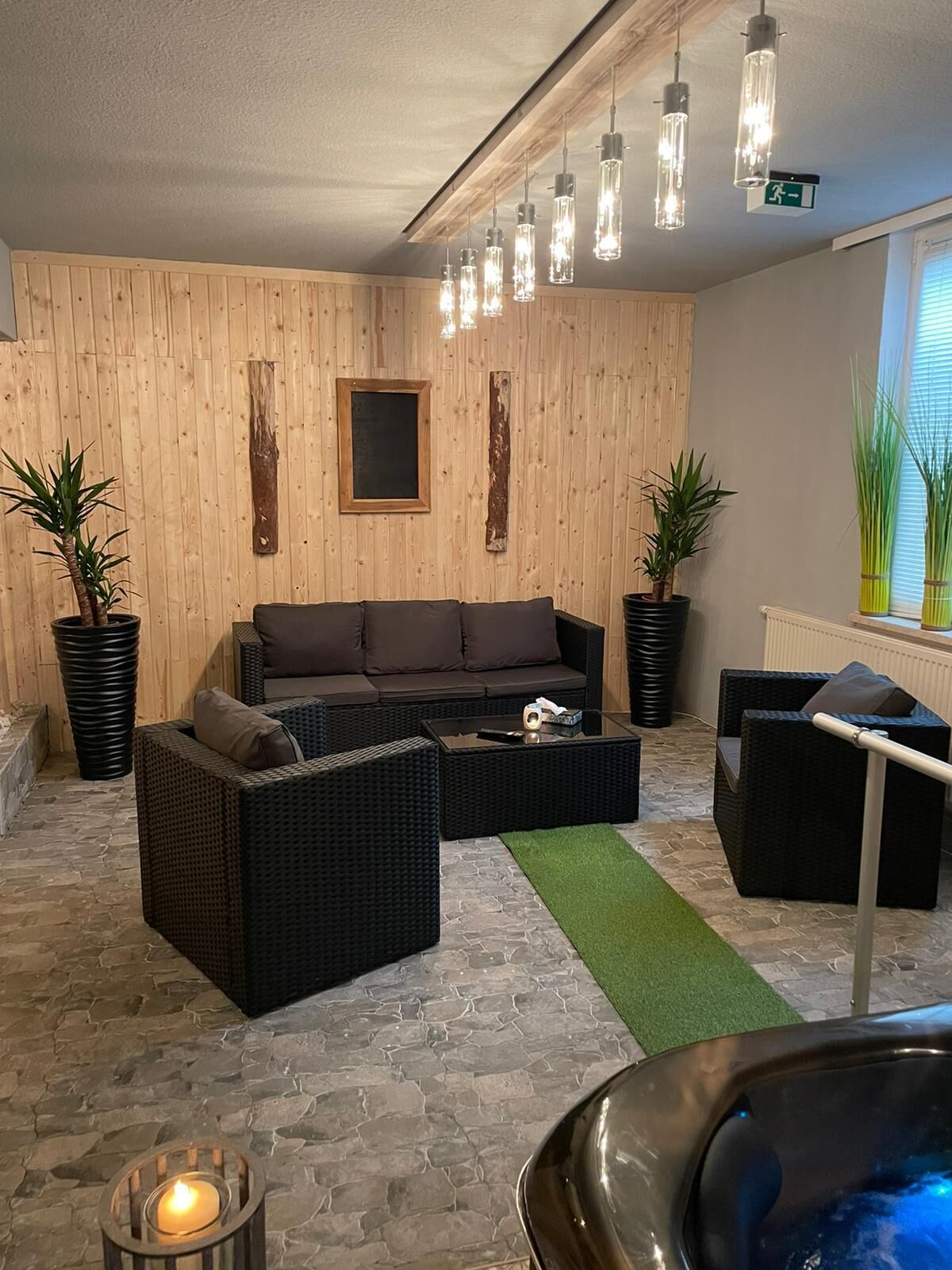Ein moderner Loungebereich mit einer Holzwand, einem Sofa, zwei Sesseln, einem Couchtisch und Topfpflanzen.