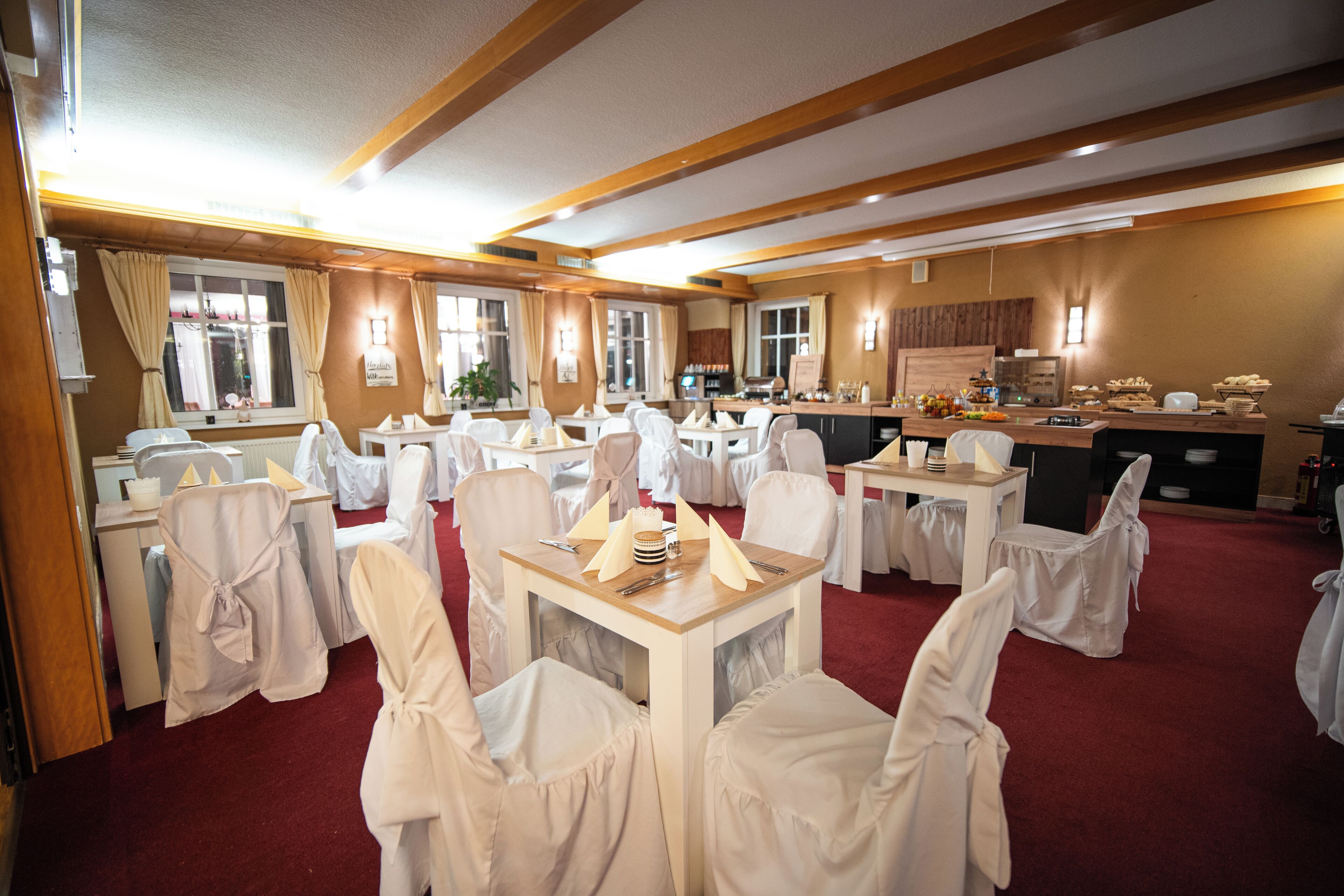 Un salón de banquetes con mesas dispuestas para un evento formal, con sillas y mesas blancas, y una alfombra roja.