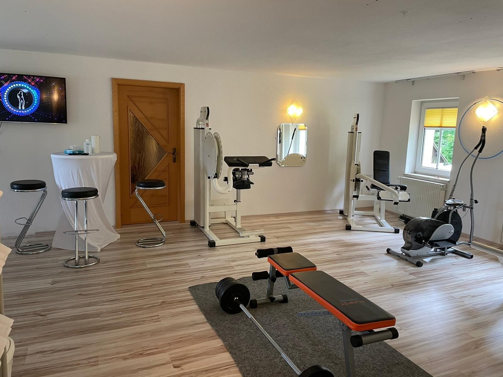 A home gym with a treadmill, stationary bike, bench press, and weight bench.