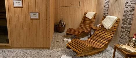 Un spa con paredes de madera, tres tumbonas de madera, suelo de baldosas de piedra y carteles que indican distintos servicios de masaje.