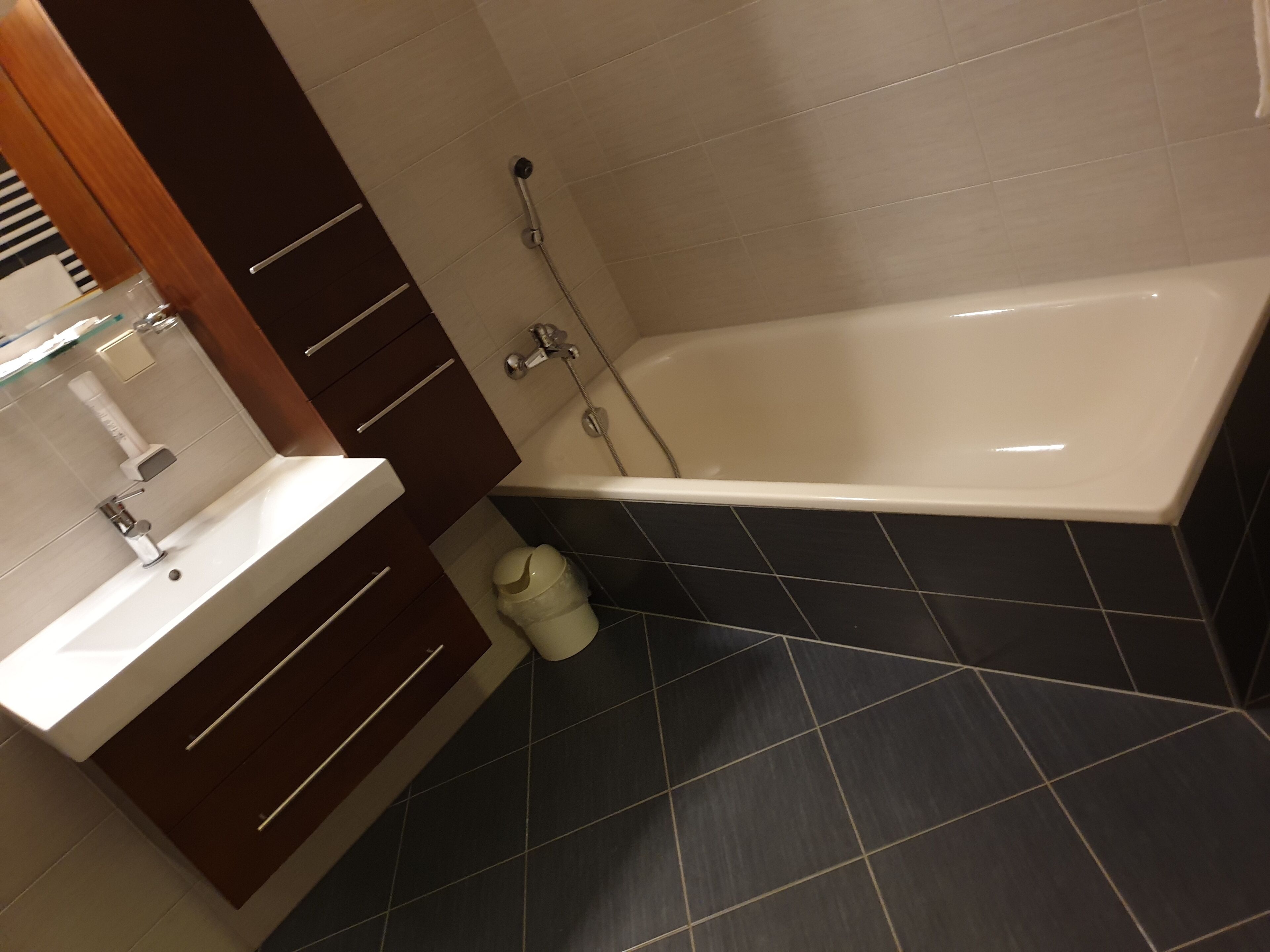 Un baño con bañera, lavamanos y piso de baldosas oscuras.