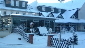 A snow-covered building with multiple windows, a glass entrance, and a brick entrance gate.