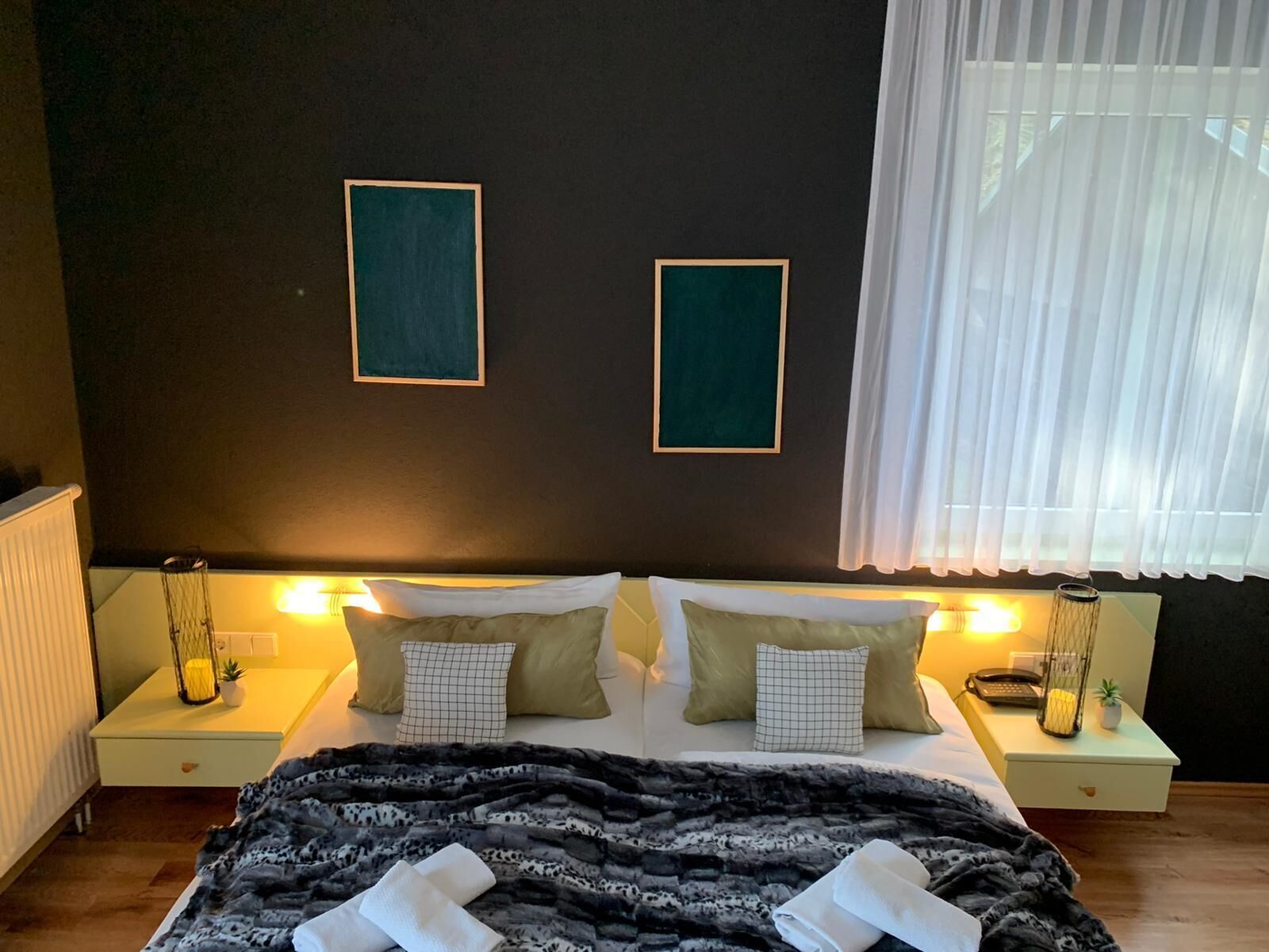Un dormitorio con una cama, dos mesitas de noche, un radiador y una ventana con cortinas.
