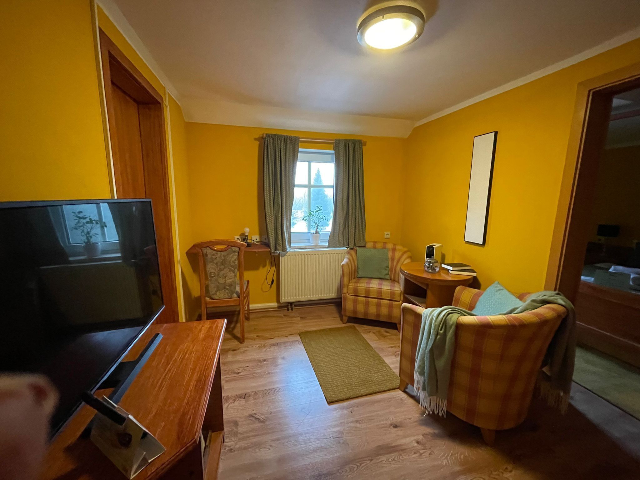 A living room with a television, a sofa, a chair, a small table, and a window with curtains.